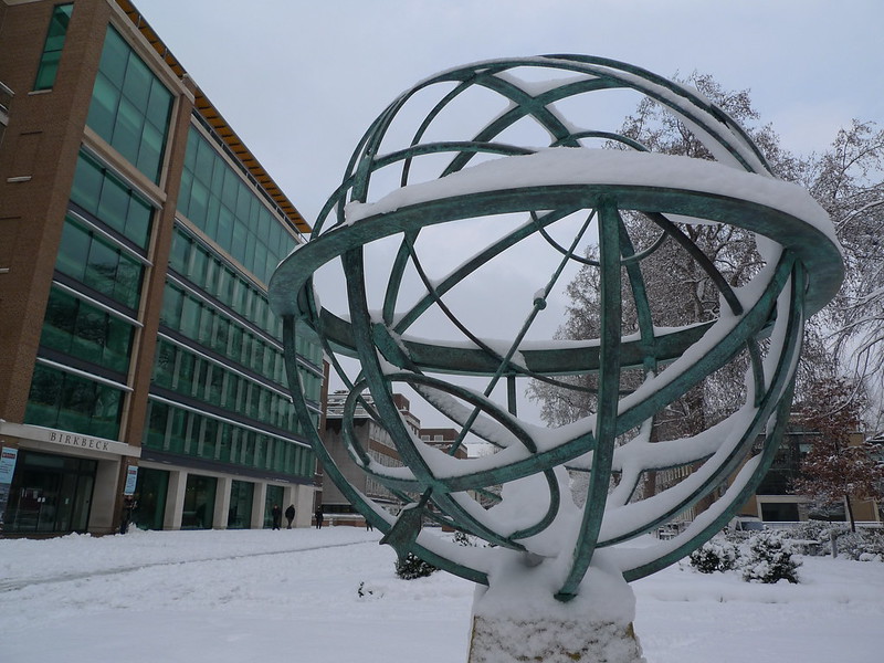 Photo of an outdoor sculpture of an abstract planet with
concentric metal circles, covered in snow, with Birkbeck,
University of London, in the background