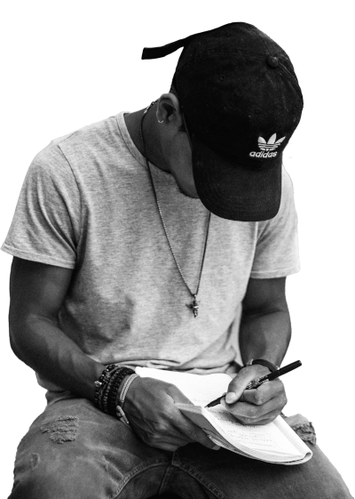 A man wearing a baseball cap, a t-shirt, and a chain around his neck,
    writing in a notebook
